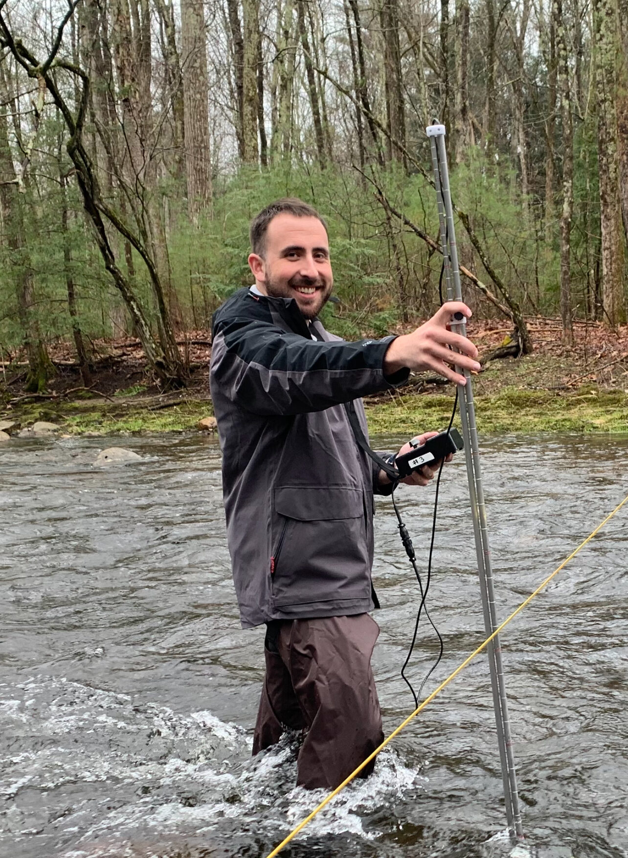 Will stands in the middle of a large stream collecting depth measurements